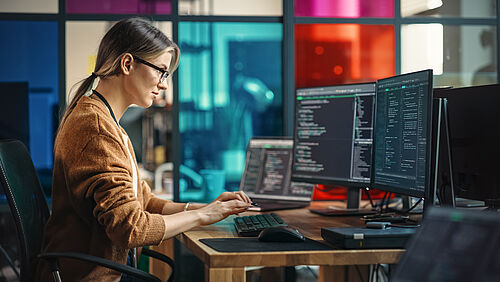 Eine Frau sitzt vor zwei Computermonitoren mit Code
