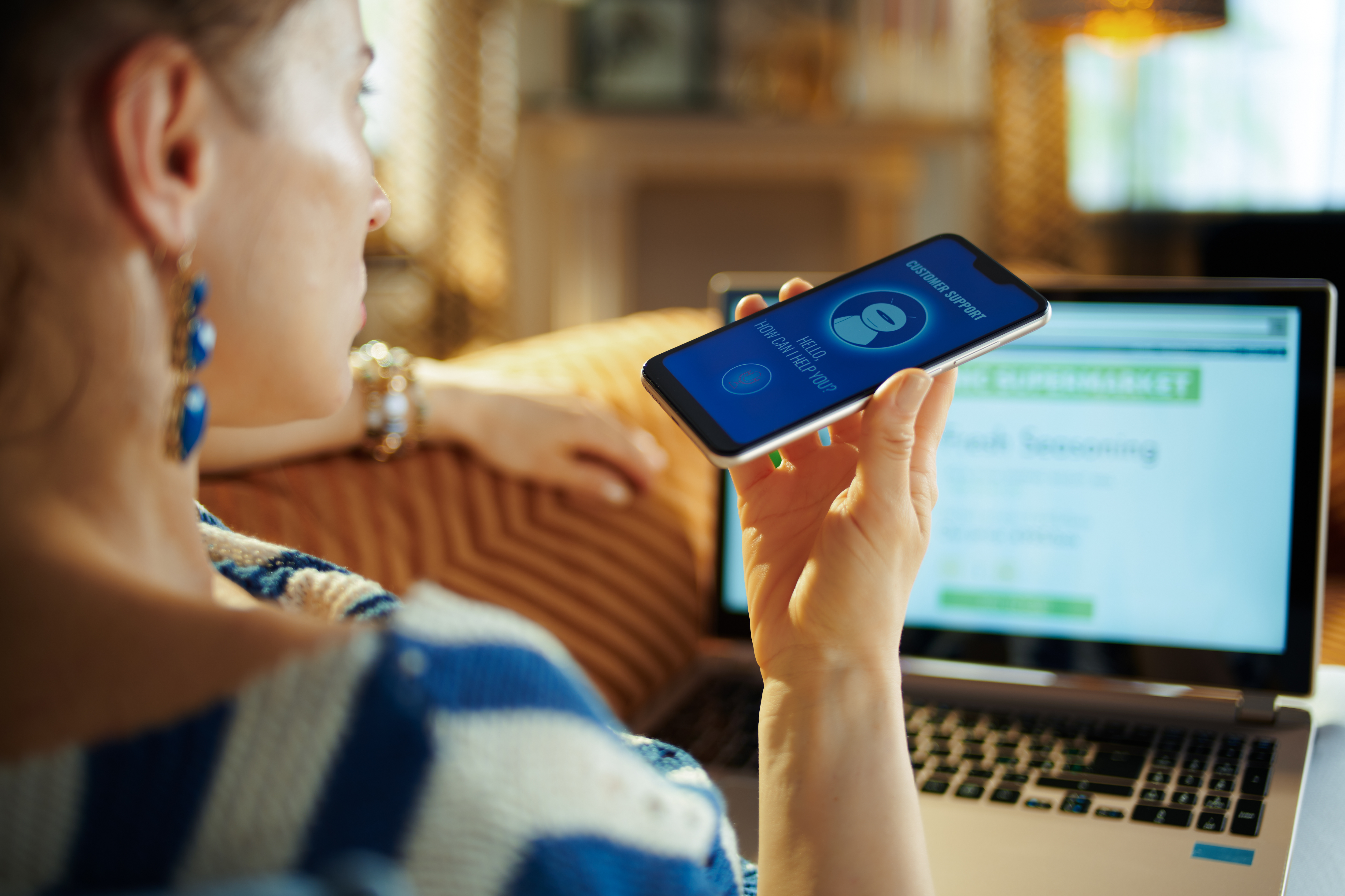 Eine Frau spricht in ihr Handy und schaut dabei auf ihren Laptop. Eine Frau spricht in ihr Handy und schaut dabei auf ihren Laptop.