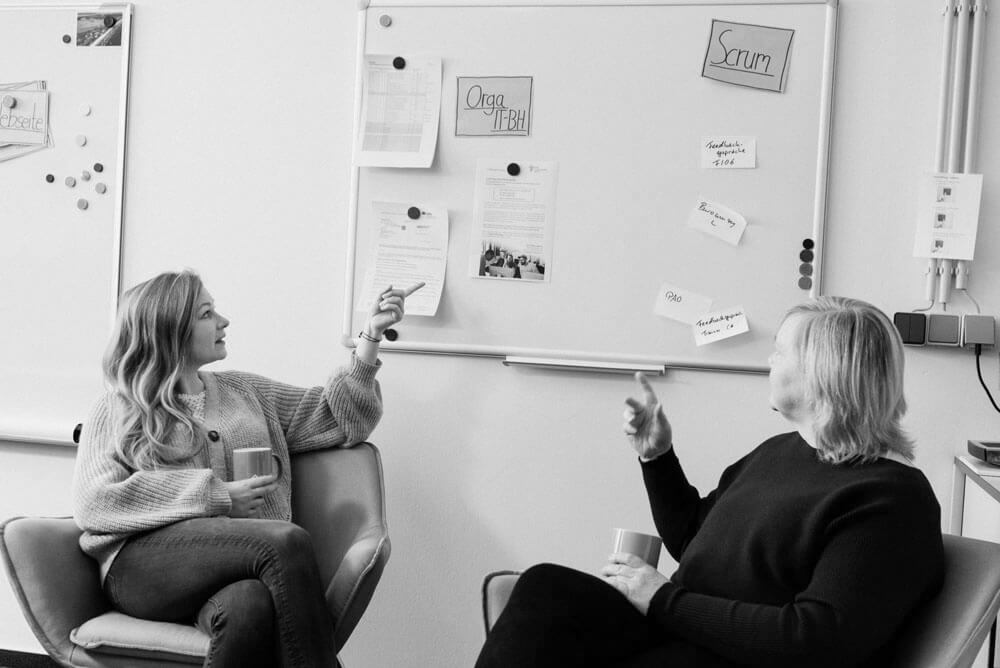 Zwei Frauen sitzen im Büro vor einem Whiteboard