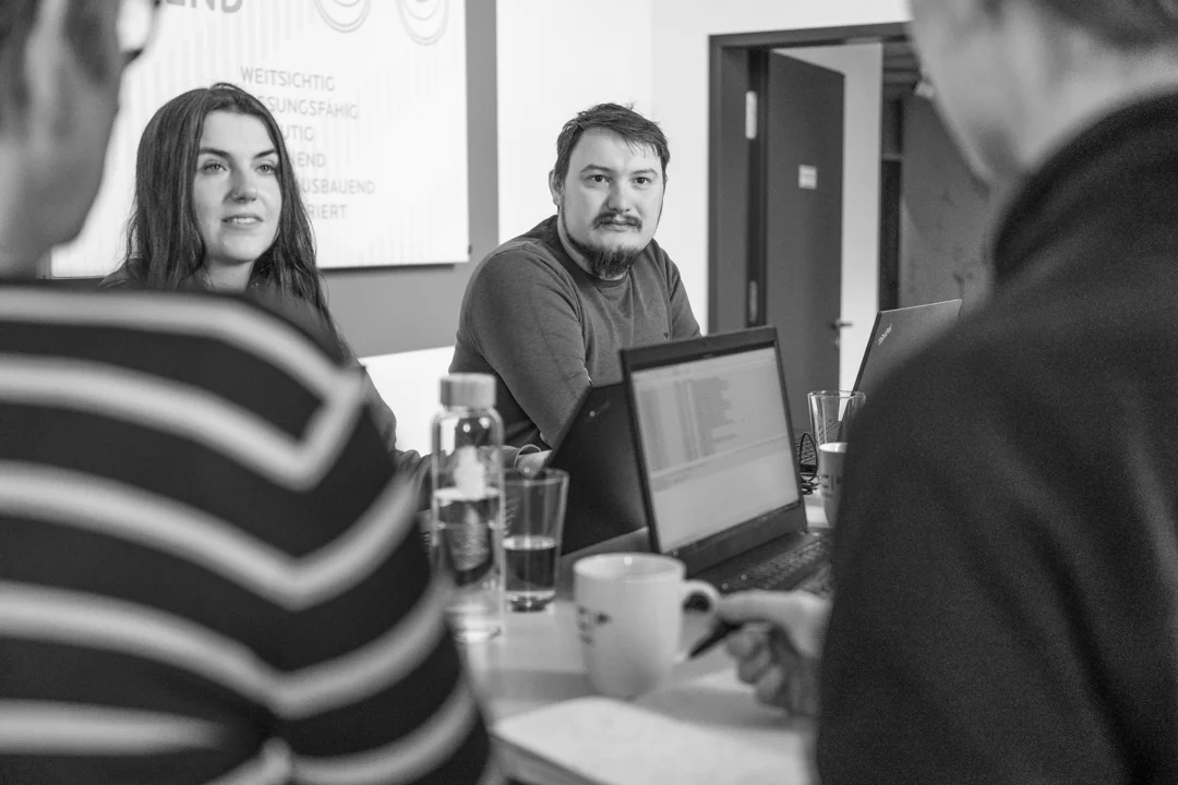 Vier Personen stehen lächelnd an einem Besprechungstisch