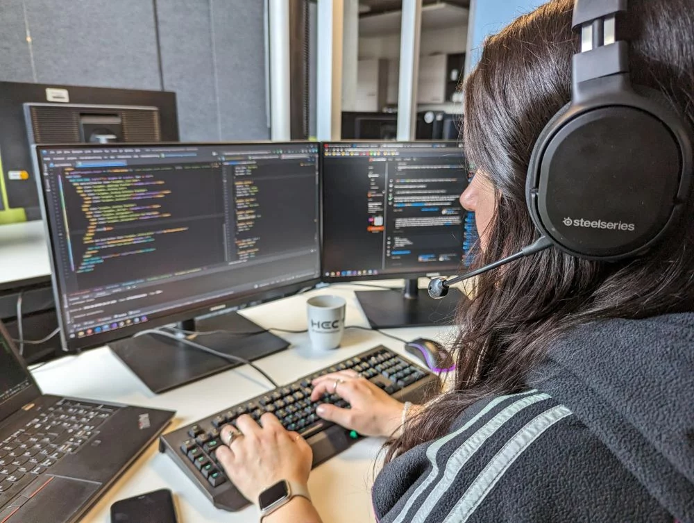 Lara sitzt mit Headset auf am Schreibtisch und programmiert