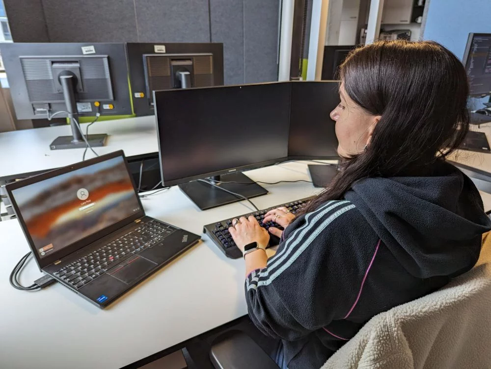 Lara sitzt an ihrem Schreibtisch im HEC Büro und meldet sich auf ihrem PC an