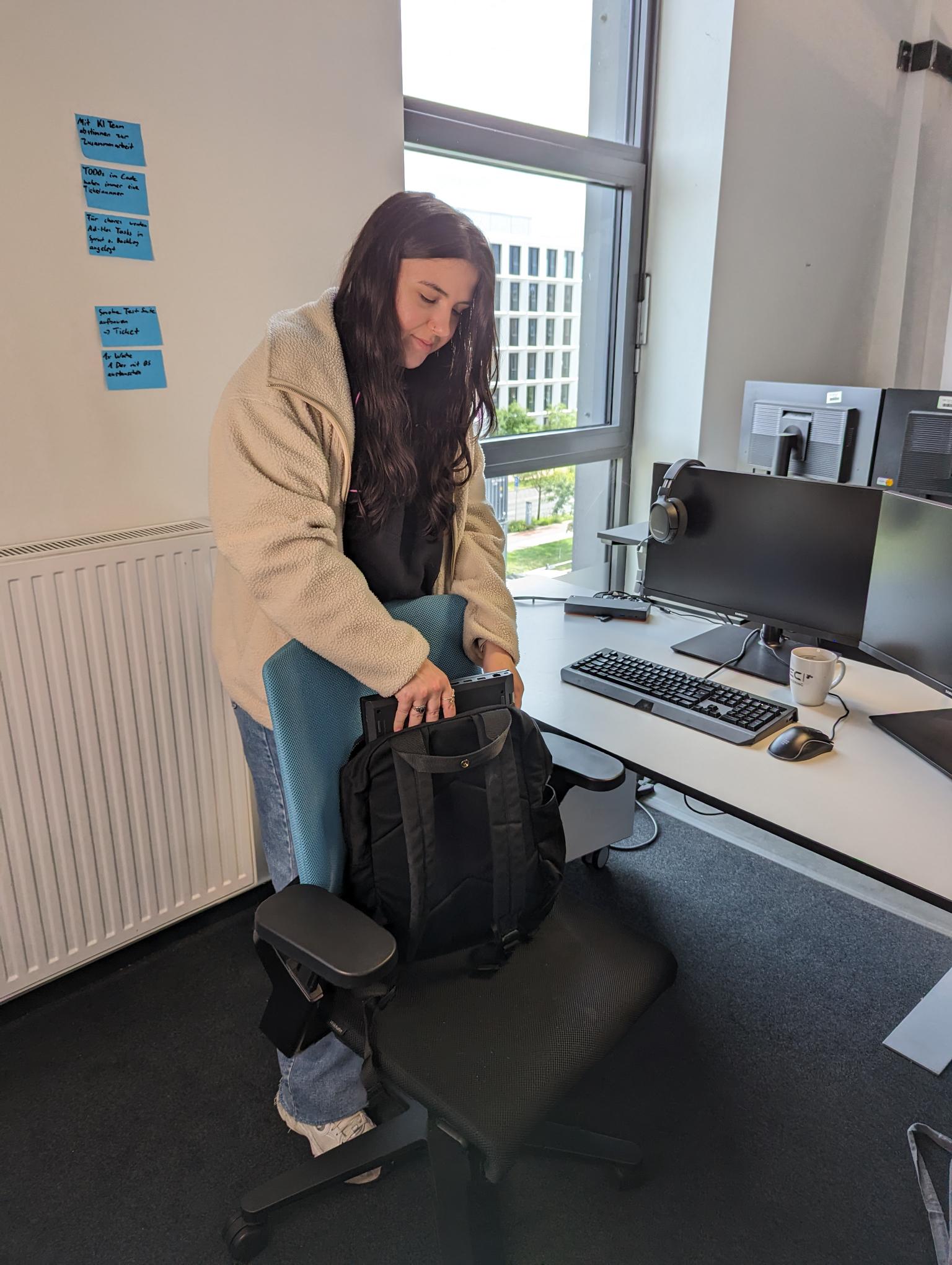 Lara steht im HEC Büro an ihrem Schreibtisch und packt ihren Rucksack 