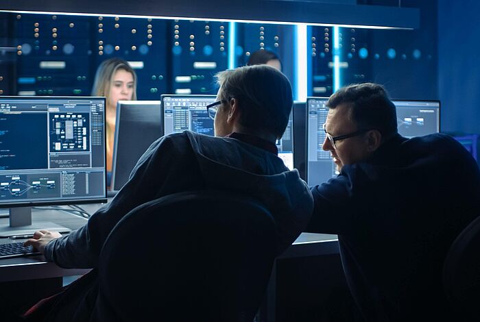 Zwei Männer sitzen vor Monitoren mit Code