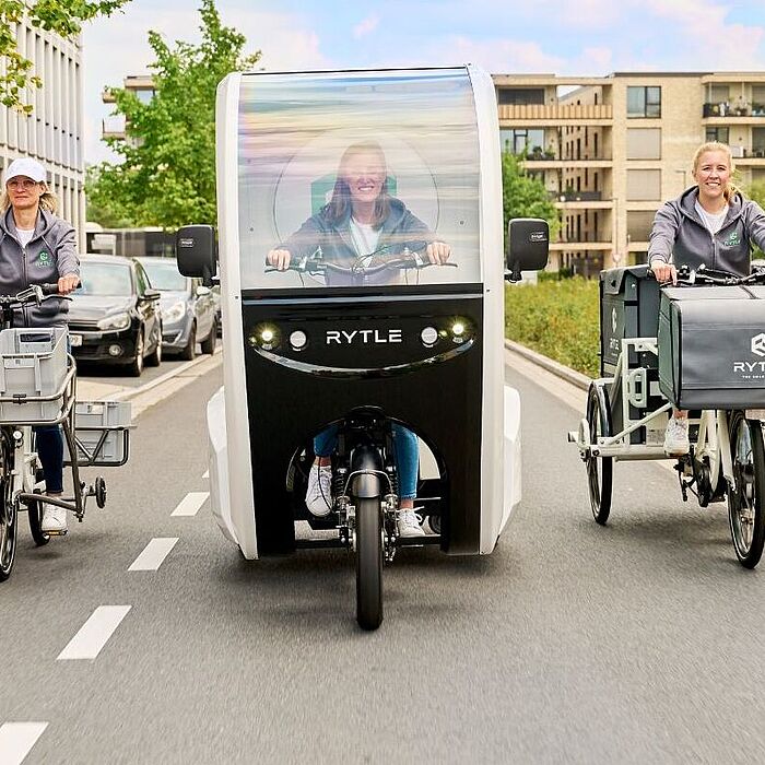 Drei verschiedene RYTLE E-Cargo-Bikes fahren auf einer Straße