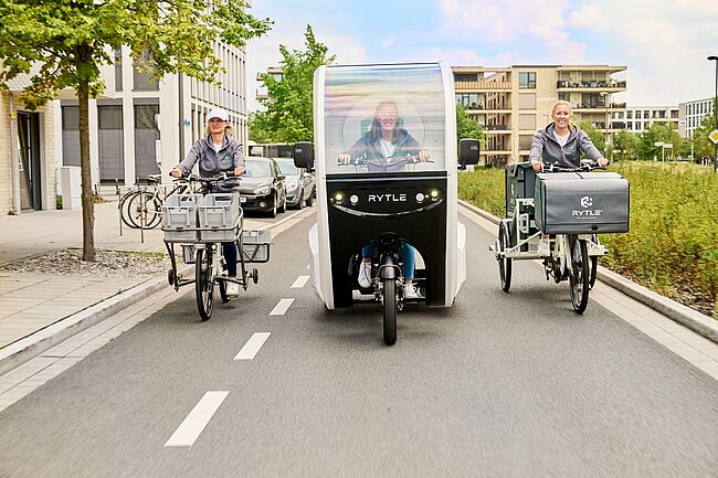 Drei verschiedene RYTLE E-Cargo-Bikes fahren auf einer Straße