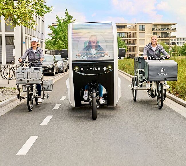 Drei verschiedene RYTLE E-Cargo-Bikes fahren auf einer Straße