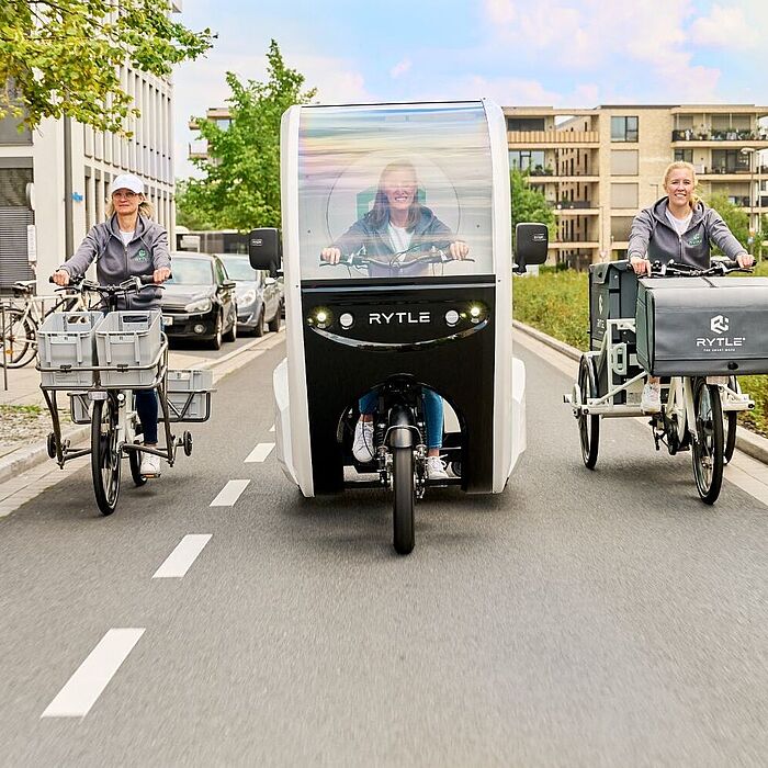 Drei verschiedene RYTLE E-Cargo-Bikes fahren auf einer Straße