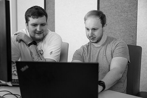Zwei Männer schauen in einen Computer Bildschirm im Büro der HEC. Sie sind fokussiert.