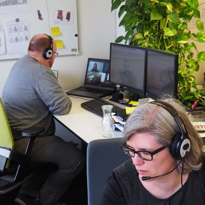 Zwei Personen mit Headsets an ihren Monitoren