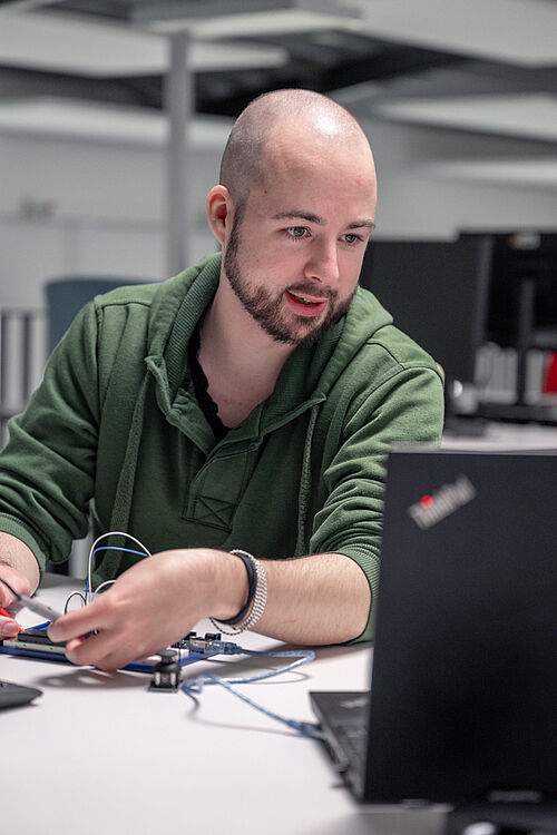 IoT-Entwickler Kevin Czesla sitzt am Schreibtisch und bearbeitet Platinen