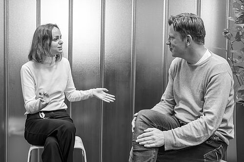 Eine Frau und ein Mann sitzen im Foyer der HEC und unterhalten sich.