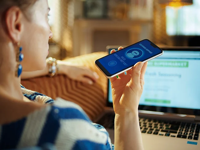 Eine Frau spricht in ihr Handy und schaut dabei auf ihren Laptop.