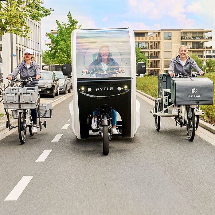 Drei verschiedene RYTLE E-Cargo-Bikes fahren auf einer Straße