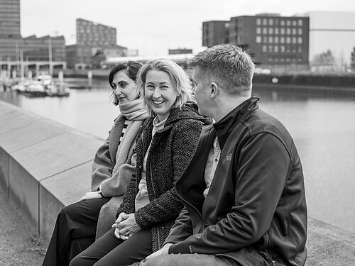 Drei Personen sitzen auf einer modernen Hafenmauer am Euopahafen in Bremen