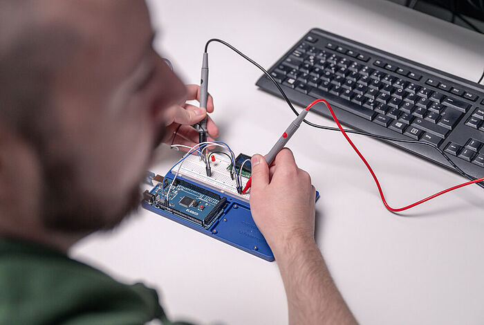 IoT-Entwickler Kevin Czesla sitzt am Schreibtisch und bearbeitet Platinen