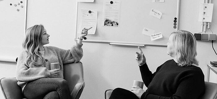 Zwei Frauen sitzen im Büro vor einem Whiteboard