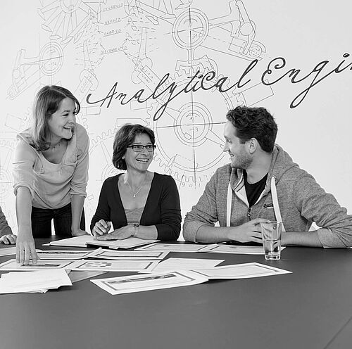 Besprechung mit vier Teilnehmenden an einem großen Tisch