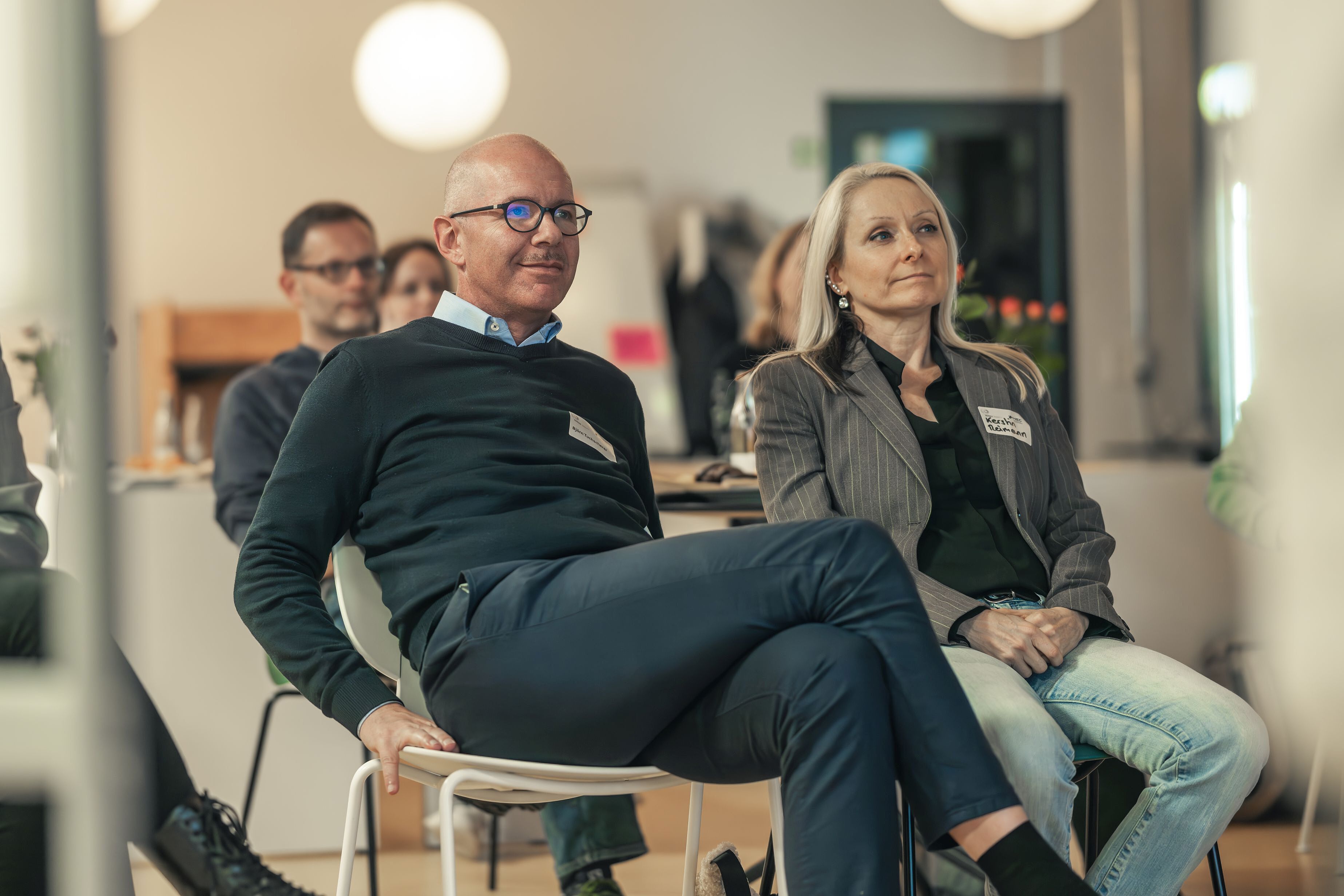 Zwei Männer und eine Frau sitzen auf einem Stuhl und hören einem Vortrag zu.