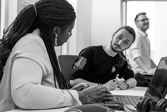 Zwei junge Entwickler:innen diskutieren vor ihren Laptops