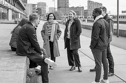 Mehrere Personen stehen lachend auf dem Gehweg an einer Hafenmauer am Euopahafen in Bremen