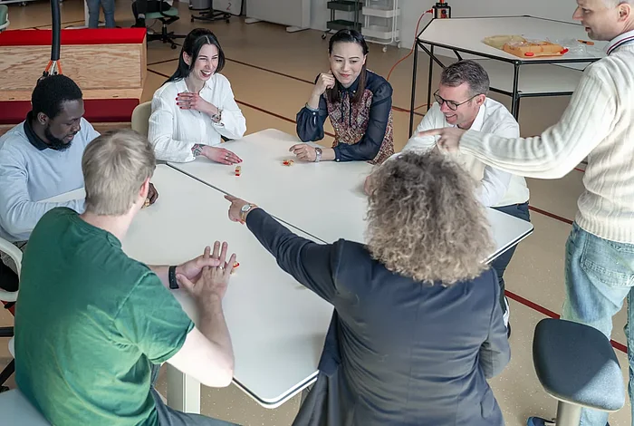 Mehrere Menschen sitzen um einen Tisch in einem Workshopraum im Bürogebäude Schuppen Eins und reden miteinander.