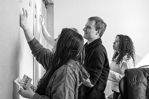 Mehrere Personen stehen im Büro der HEC an einem Raumteiler, den sie mit beschriebenen Klebezetteln bestücken. 