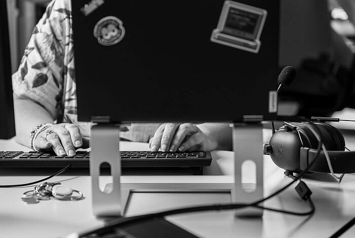 augeklapptes Laptop, dahinter die Hände einer Frau an der Tastatur herangezoomt