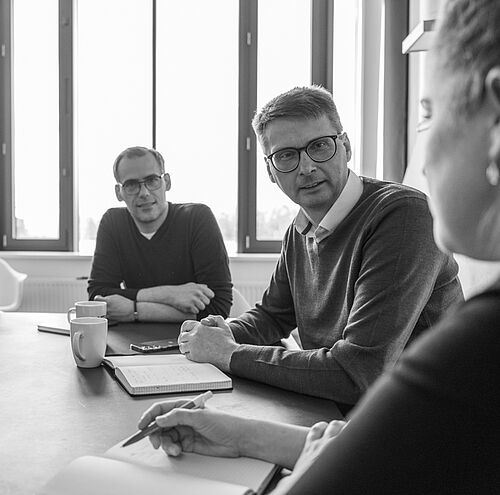 Mehrere Personen sitzen an einem großen Besprechungstisch mit Sonnenlicht.