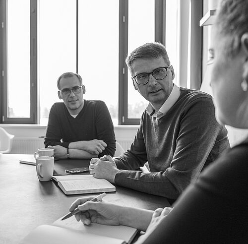 Mehrere Personen sitzen an einem großen Besprechungstisch mit Sonnenlicht.