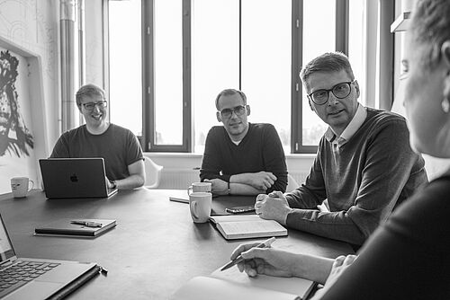 Mehrere Personen sitzen an einem großen Besprechungstisch mit Sonnenlicht.