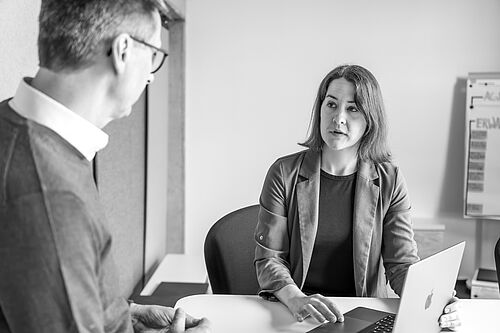 Eine Frau und ein Mann an einem Stehtisch. Sie hält ihren Laptopbildschirm.