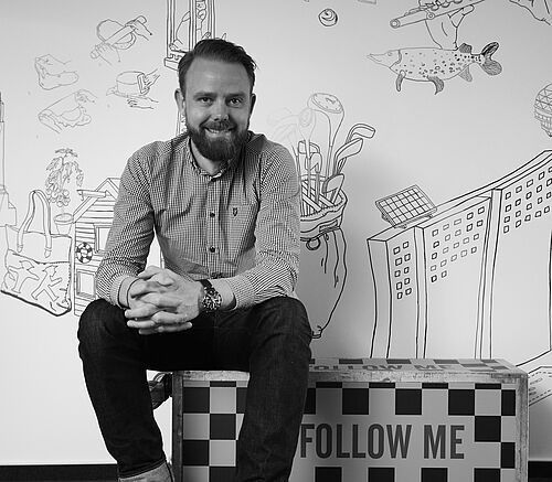 Ein Mann sitzt auf einem umgekippten Flugzeugservierwagen und lächelt