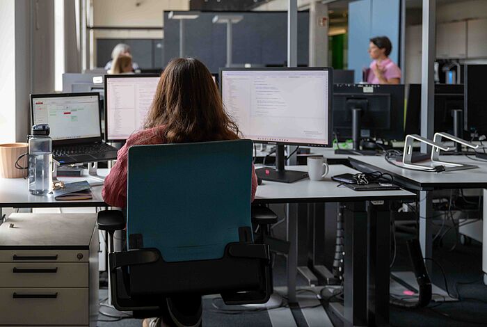 Ein Raum mit Arbeitsplätzen, eine Frau sitzt an einem Computer
