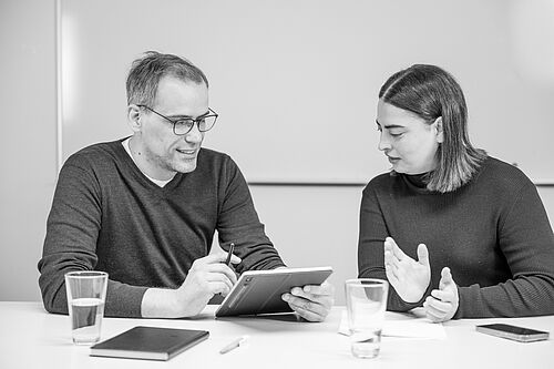 Ein Mann und eine Frau sitzen an einem Besprechungstisch und haben eine Diskussion vor einem Whiteboard
