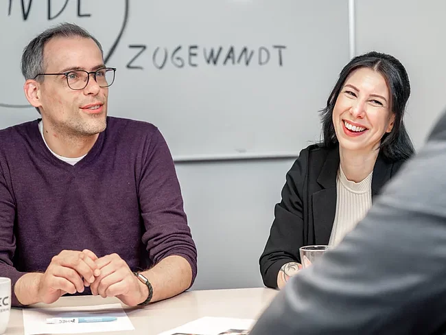 Ein Mann und eine Frau sitzen an einem Besprechungstisch.
