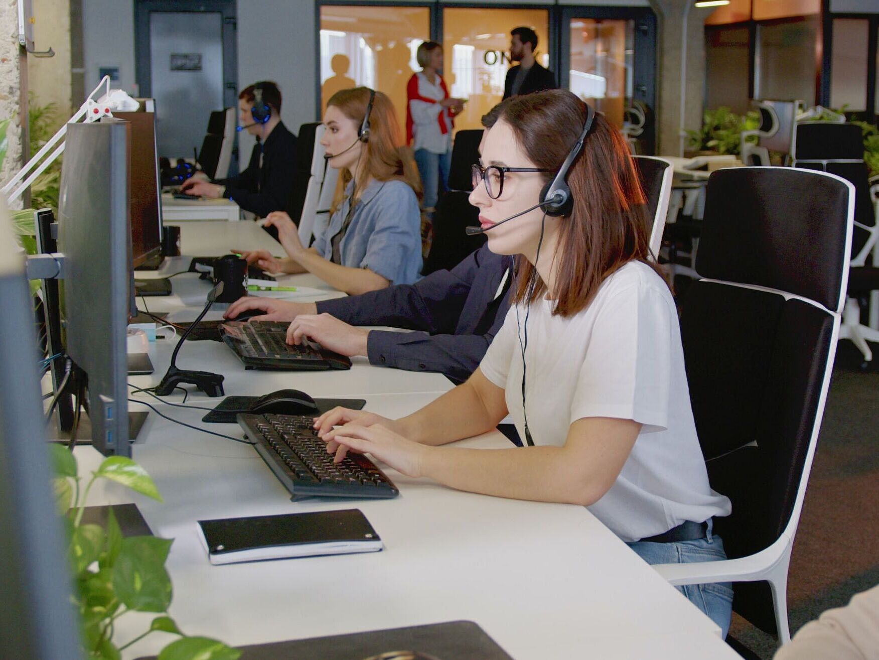 Mitarbeitende im Kundenservice Personen in einem Großraumbüro mit Headsets
