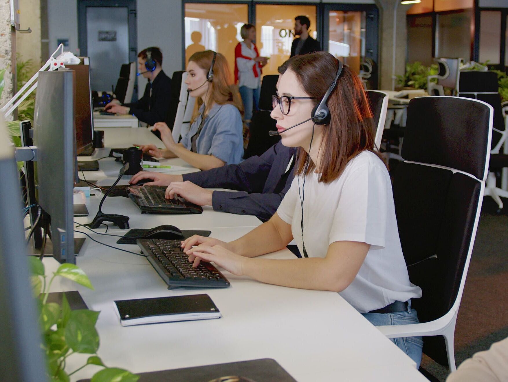 Mitarbeitende im Kundenservice Personen in einem Großraumbüro mit Headsets