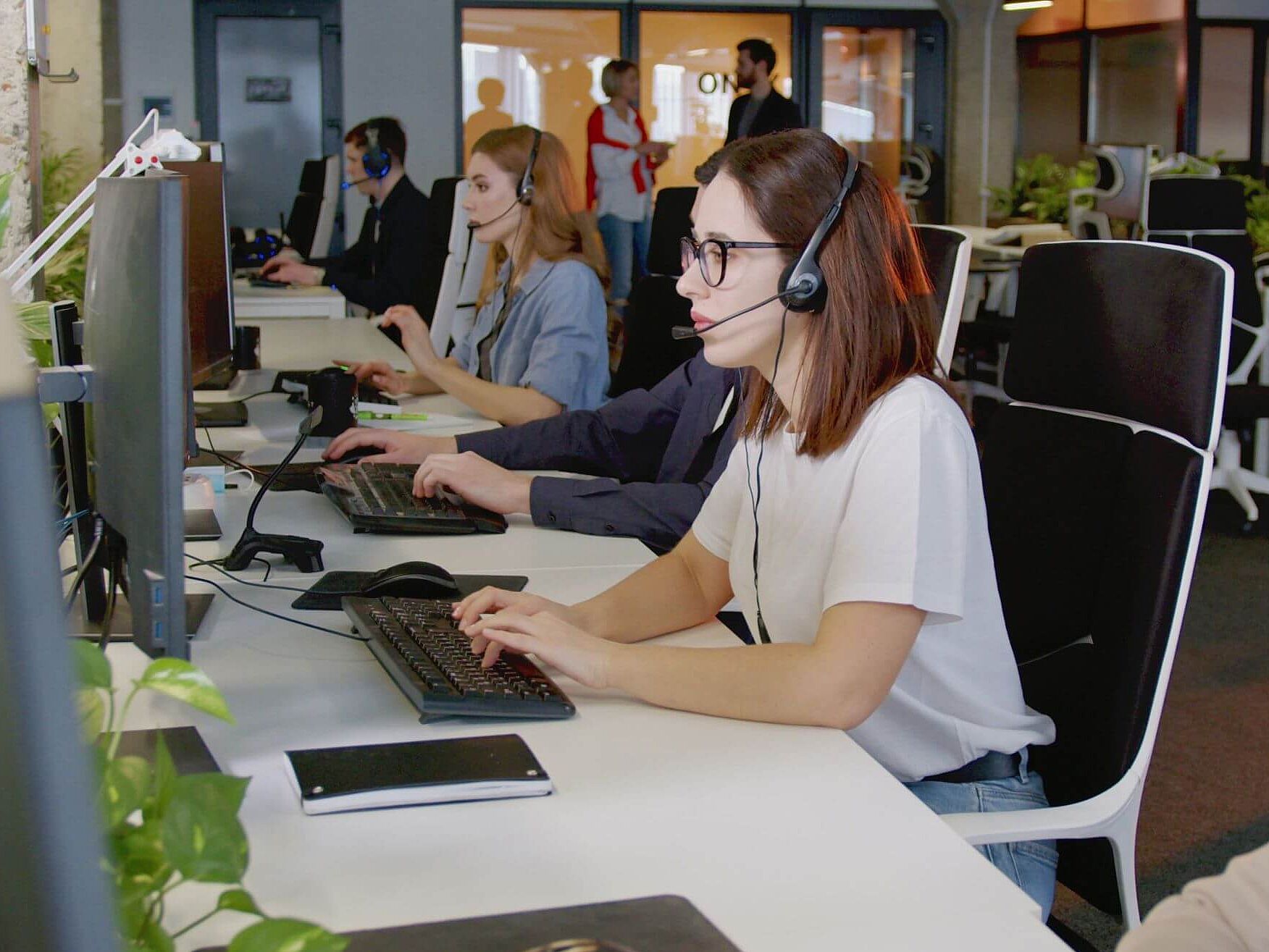 Mitarbeitende im Kundenservice Personen in einem Großraumbüro mit Headsets