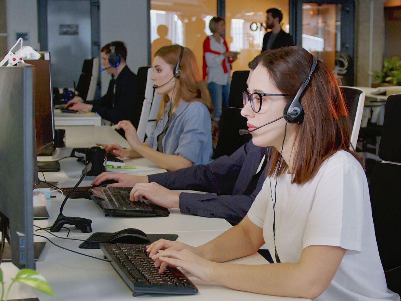 Mitarbeitende im Kundenservice Personen in einem Großraumbüro mit Headsets