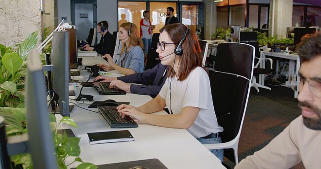 Personen in einem Großraumbüro mit Headsets