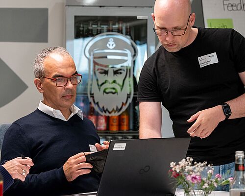 Zwei Männer suchen am Laptop nach der richtigen Einstellung für eine barrierefreie Nutzung einer Website.