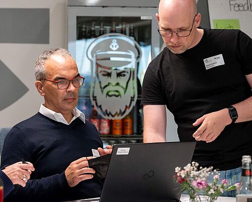Zwei Männer suchen am Laptop nach der richtigen Einstellung für eine barrierefreie Nutzung einer Website.