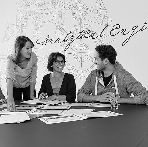 Besprechung mit vier Teilnehmenden an einem großen Tisch