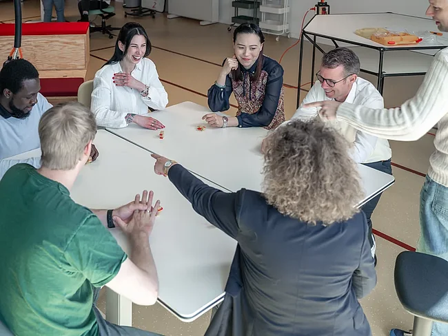 Mehrere Menschen sitzen um einen Tisch in einem Workshopraum im Bürogebäude Schuppen Eins und reden miteinander.