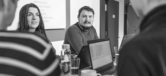 Vier Personen stehen lächelnd an einem Besprechungstisch