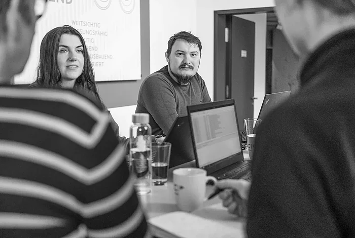 Vier Personen stehen lächelnd an einem Besprechungstisch