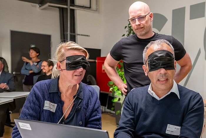 Eine Frau und ein Mann versuchen am Laptop, mit verbundenen Augen online ein Sofa zu bestellen.