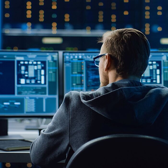 Ein Mann sitzt vor drei Computermonitoren mit Code