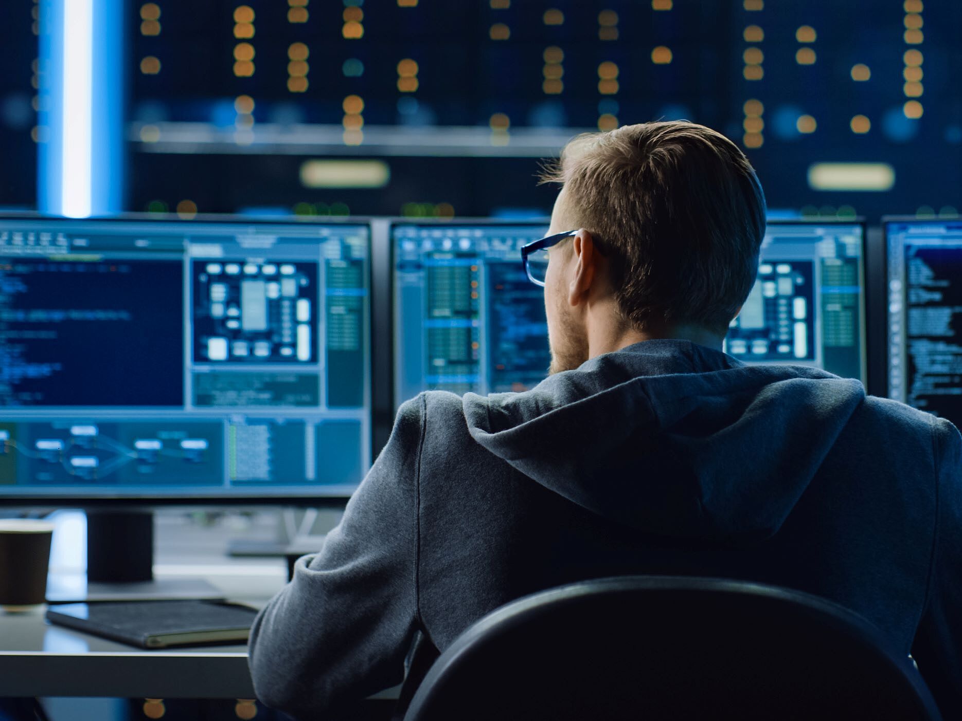 Ein Mann sitzt vor drei Computermonitoren mit Code